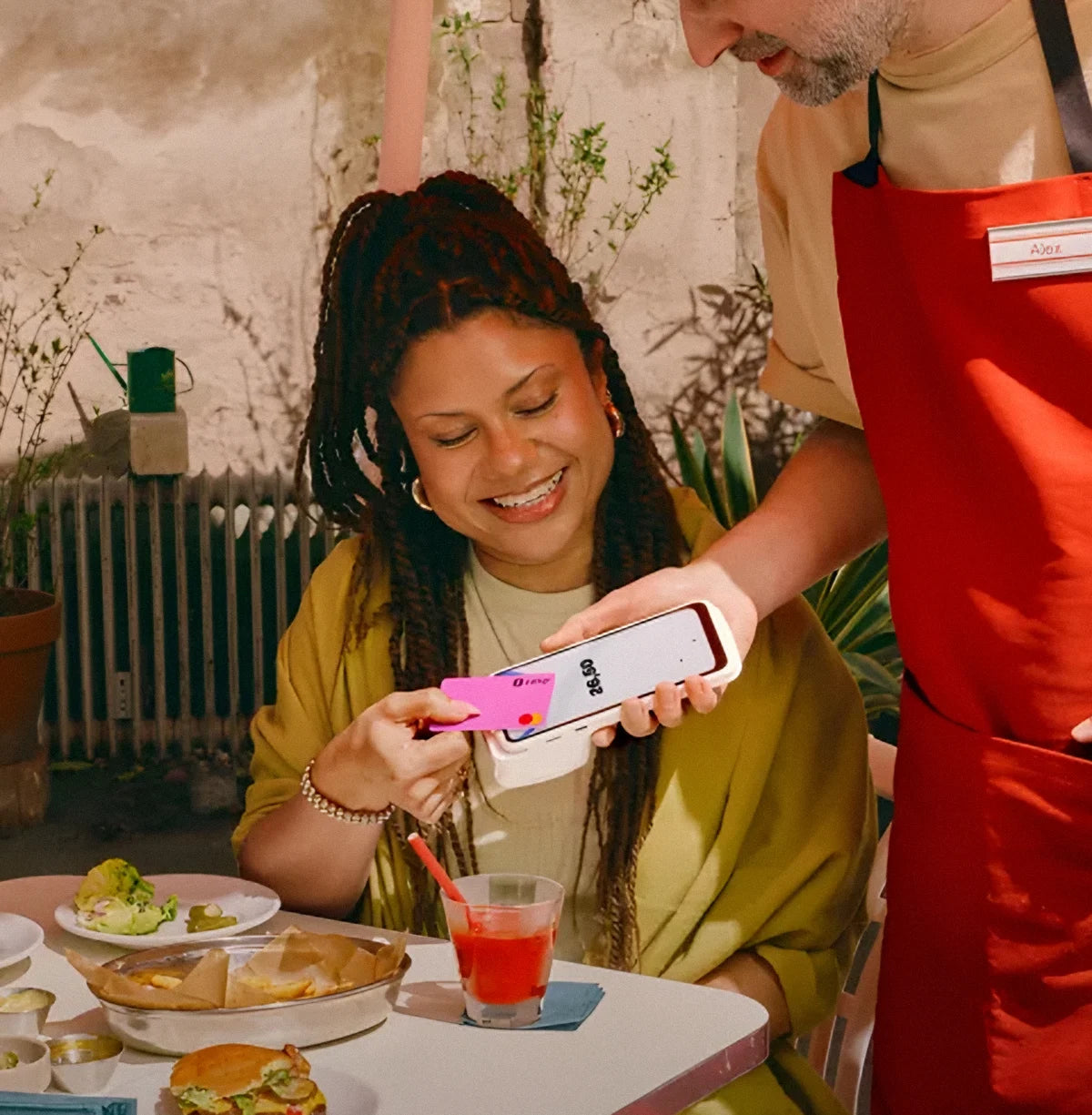 A smiling customer makes a contactless card payment on the SumUp Terminal held out by the waiter